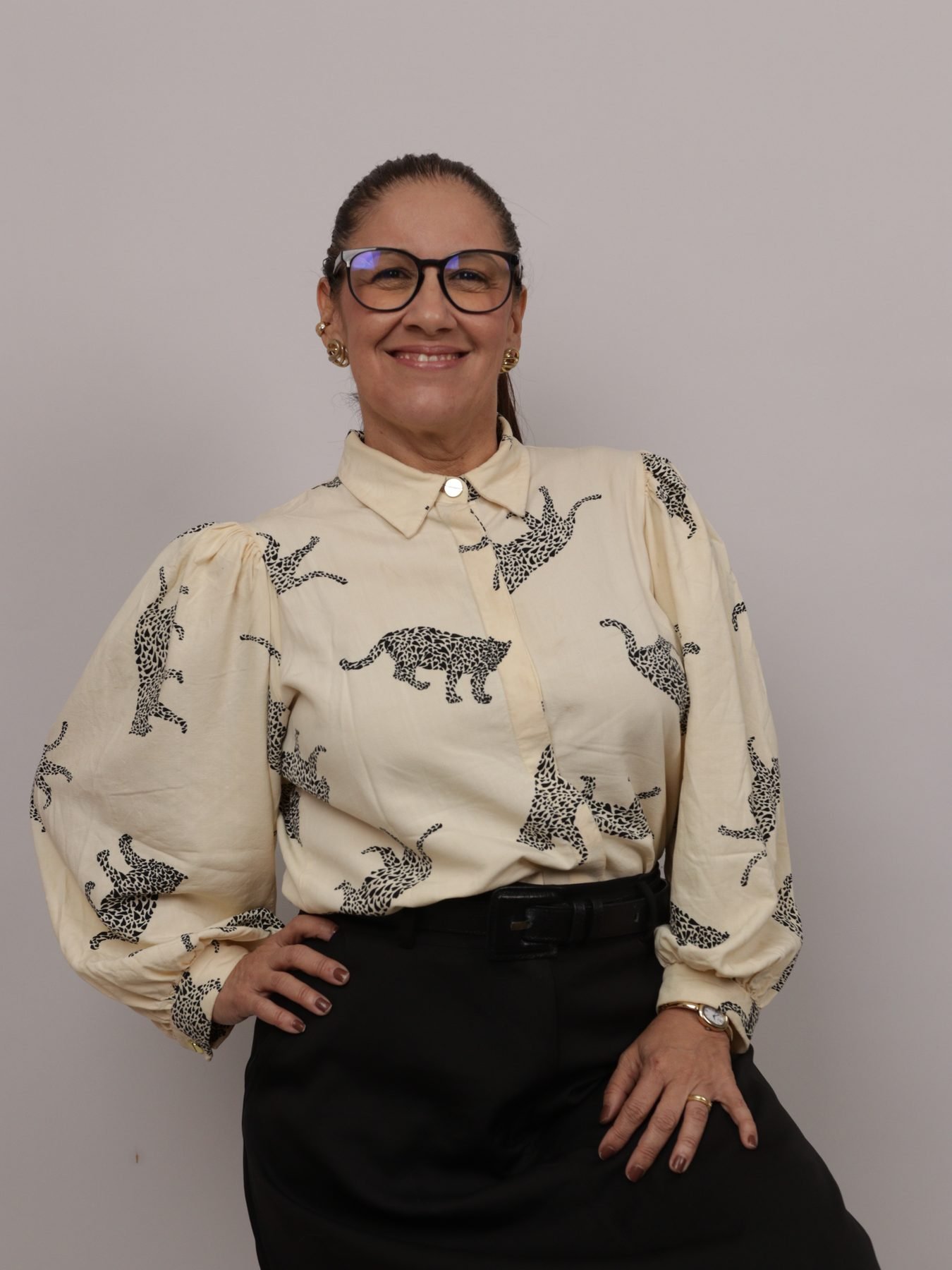 Retrato de Débora Gomes, fonoaudióloga da Longevus, sorrindo, com camisa estampada em tons claros, óculos e fundo neutro.